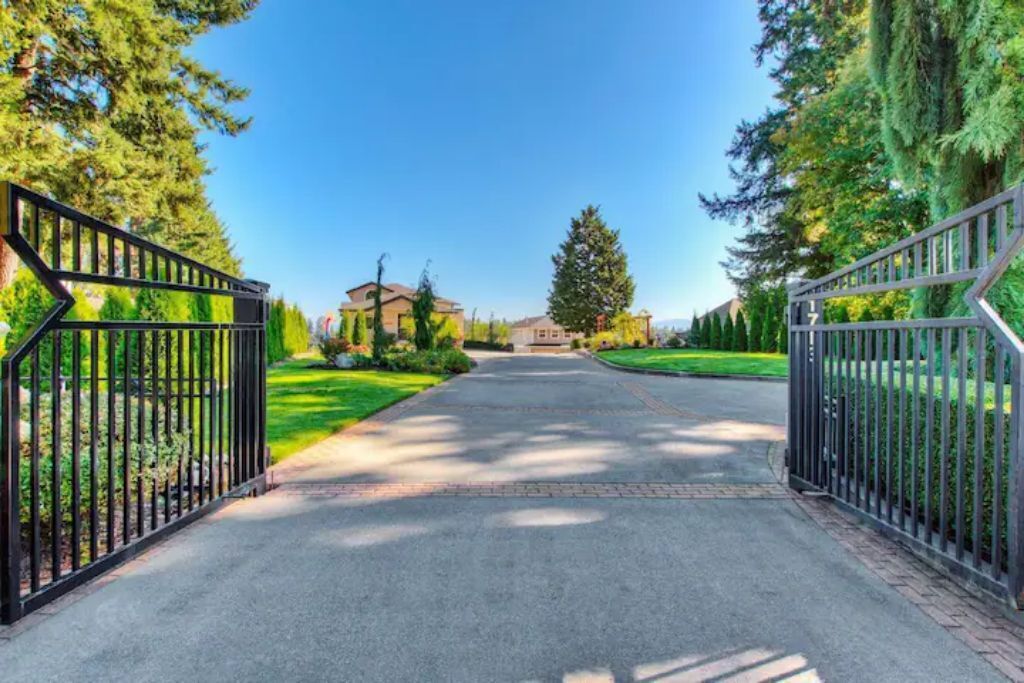 A gated driveway leading to a house with a well-maintained lawn and a large tree.