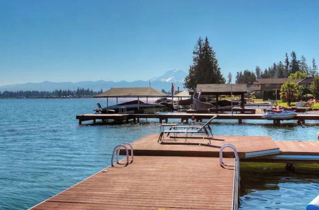 Un muelle de madera que se adentra en un lago, con vistas claras a montañas al fondo.