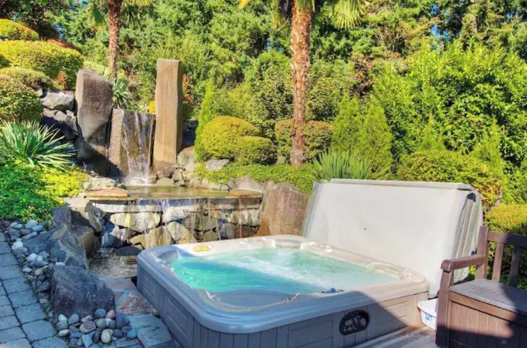 A hot tub in a garden with a waterfall and lush greenery.