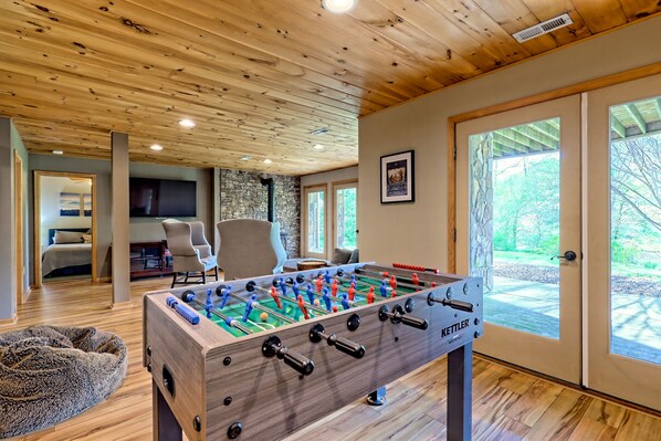 A cozy room with a foosball table, a stone fireplace, and a large window overlooking a deck.