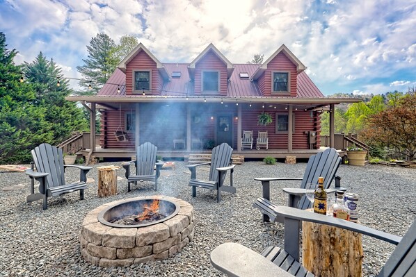 Una cabaña de troncos con un hogar de piedra y sillones Adirondack en el frente.