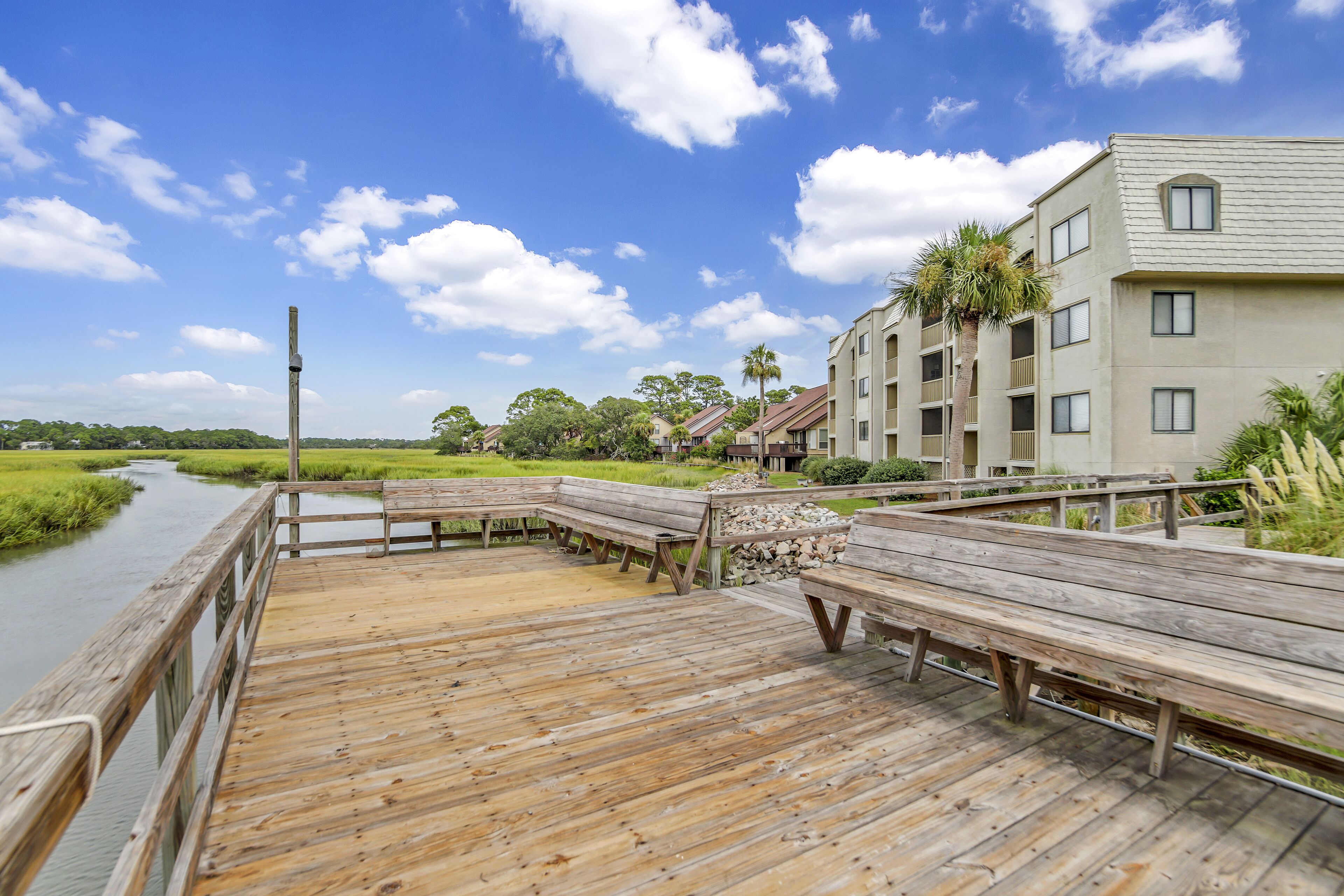 A wooden boardwalk with benches, a river, and a building with multiple balconies and windows.