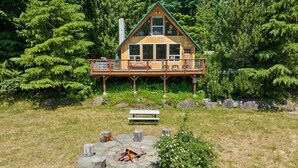 Eine Hütte mit einer Terrasse, einer Feuerstelle und einem Picknicktisch inmitten von Bäumen.