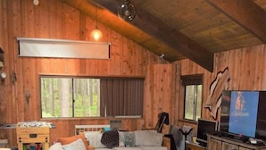 A cozy cabin-style room with wooden walls and floors, a sofa, a chair, a television, and a fireplace. - The Lodge on Shawnee Trail | Wifi, Hot tub (Packwood)
