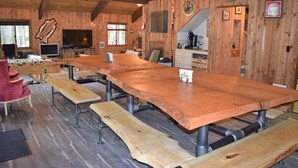 A rustic wooden interior with a long dining table, benches, a television, and a kitchen area. - The Lodge on Shawnee Trail | Wifi, Hot tub (Packwood)
