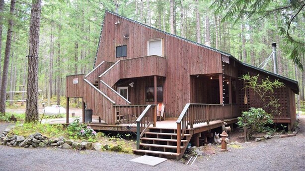 A rustic cabin with a wooden exterior, a front porch, and a staircase leading to the entrance. - The Lodge on Shawnee Trail | Wifi, Hot tub (Packwood)