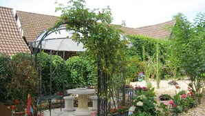 Un jardin agrémenté d’une pergola, de tables en pierre et de plantes en pot.