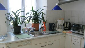 Une cuisine avec des meubles blancs, un évier, une machine à café, un grille-pain et deux plantes en pot.