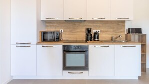 Une cuisine moderne avec des armoires blanches, un plan de travail en bois, un four encastré, une machine à café et un four à micro-ondes.
