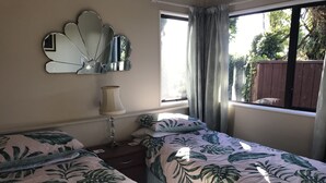A bedroom with two beds, a bedside lamp, a mirror, and a window with curtains.