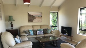 A living room with a beige sofa, a glass coffee table, a TV on a stand, and a painting on the wall.