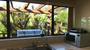 A kitchen with a double sink, a microwave, and a view of a garden through a window.