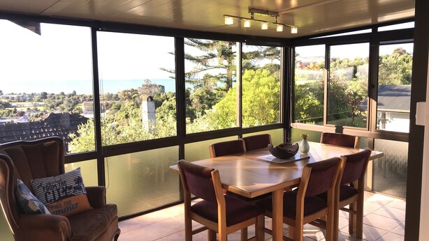 A dining area with a large table and chairs, large windows with a view of greenery and buildings, and a ceiling with recessed lighting.