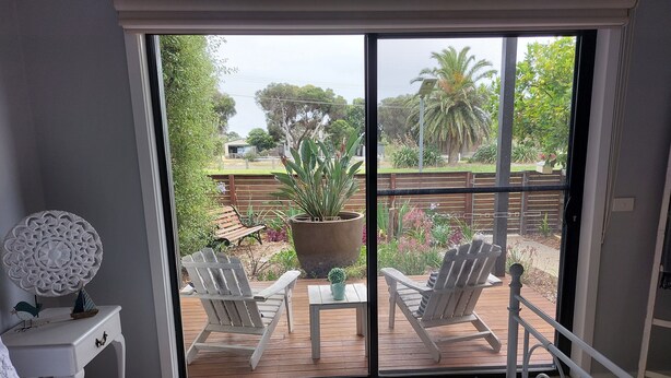 Ein Schlafzimmer mit einer großen Schiebeglastür, die auf eine Außenpatio mit zwei weißen Stühlen, einem Tisch und einem Blumentopf führt.