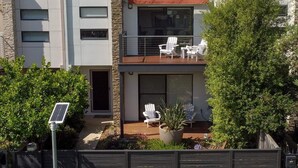 Ein modernes, zweistöckiges Haus mit Balkon, Sitzgelegenheit im Freien und einer Solaranlage.