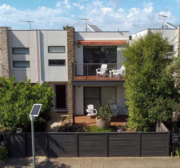 Una moderna casa a due piani con un balcone, un'area salotto esterna e un pannello solare.