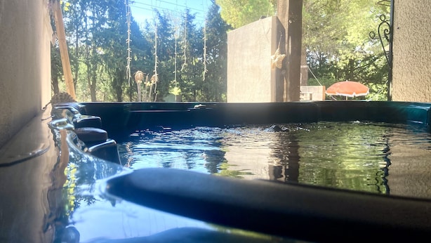 Una piscina con acqua cristallina, circondata da alberi e un pergolato in legno.