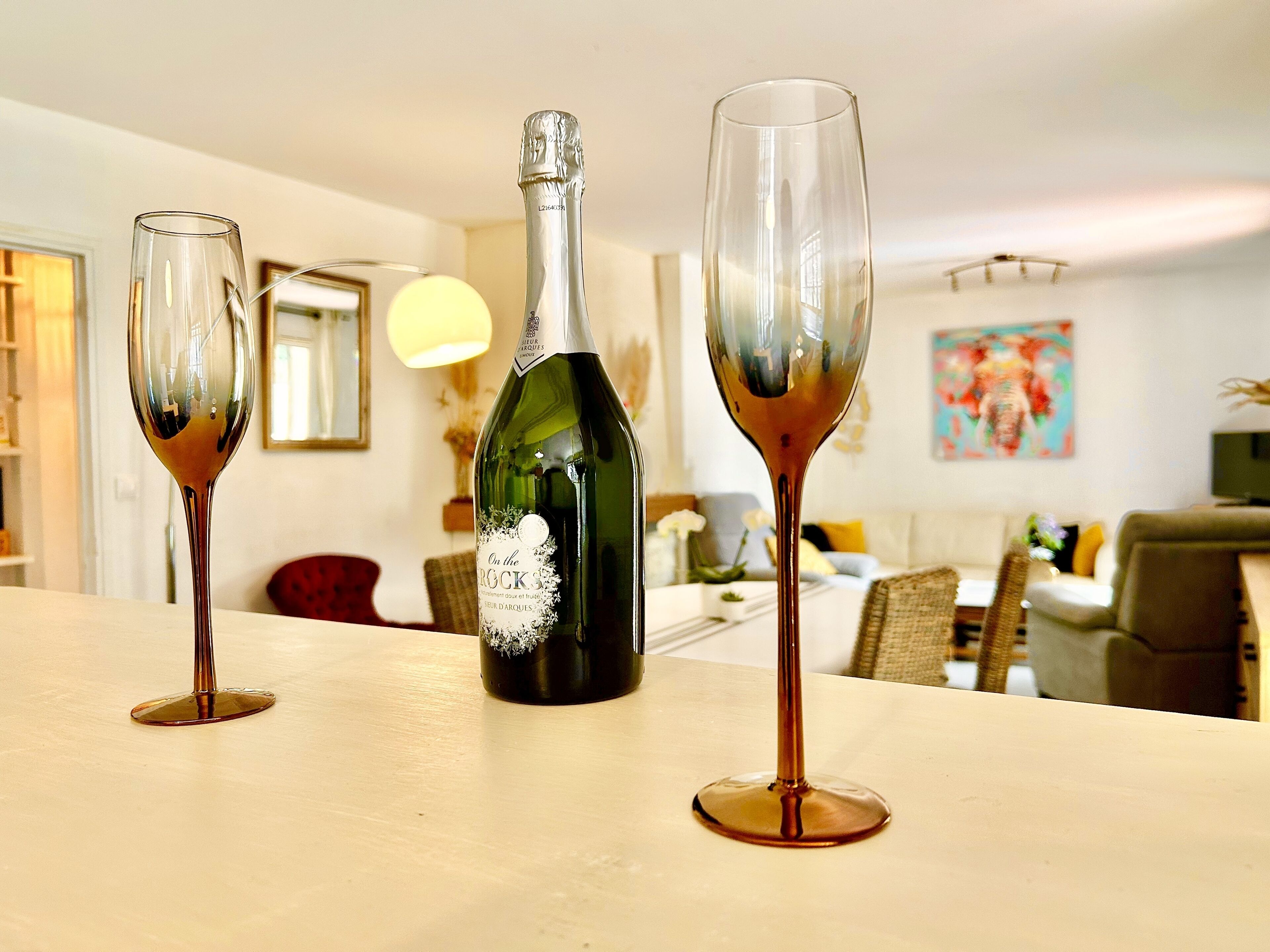 A bottle of wine and two glasses on a table in a room with a dining area in the background.