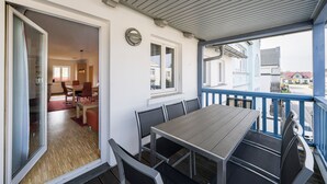 A balcony with a table and chairs, a door leading to an interior room, and a view of the street.