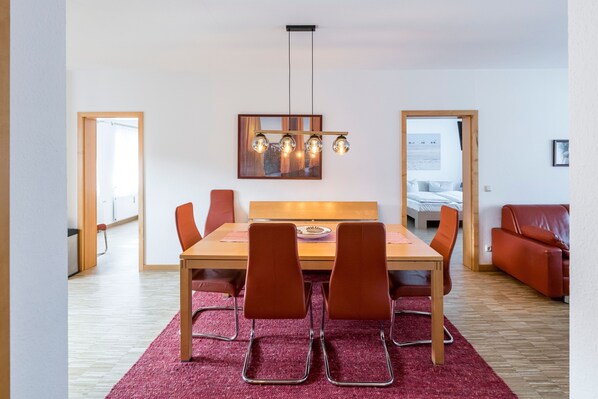 A dining area with a wooden table, four chairs, a red rug, and a pendant light fixture.