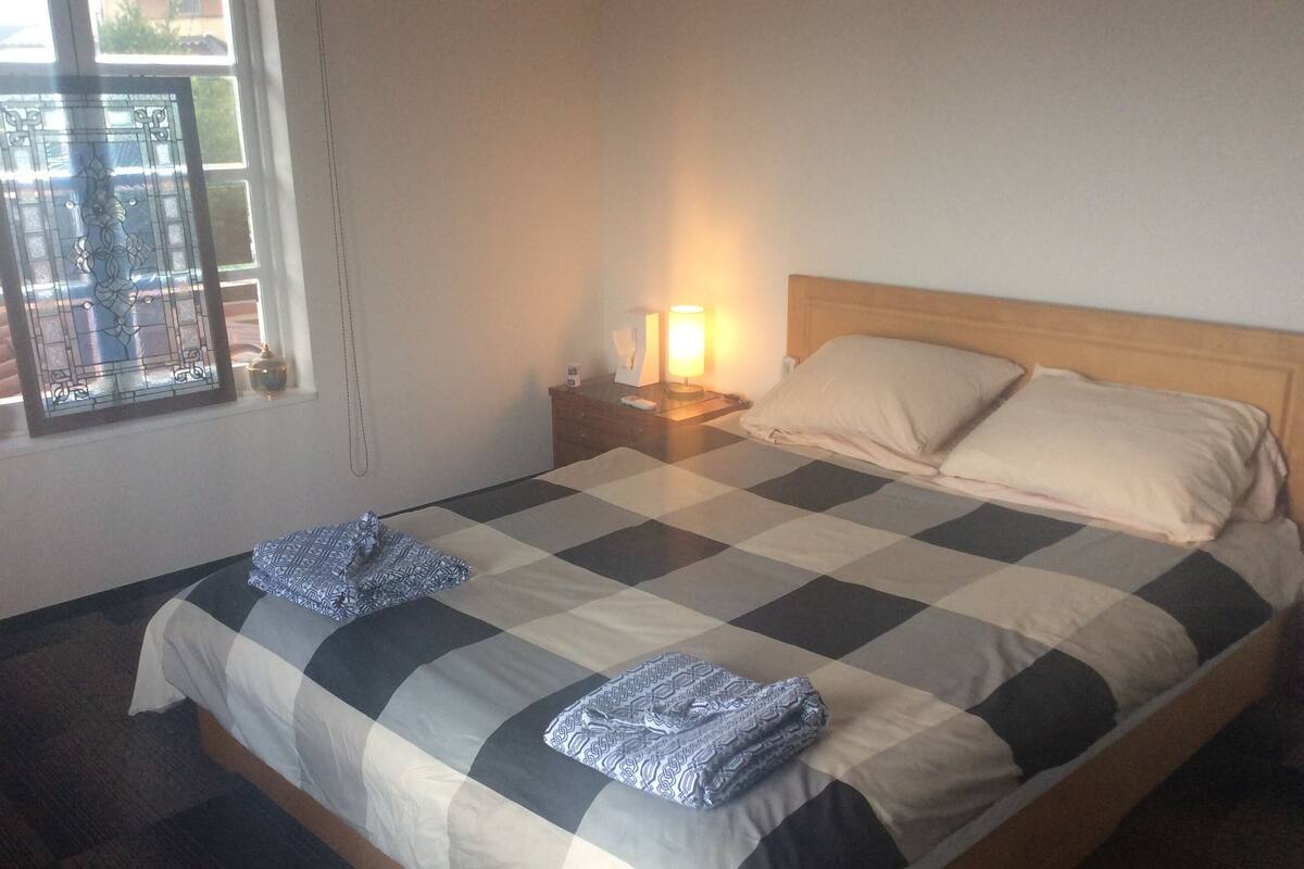 A neatly made bed with a checkered bedspread, a bedside lamp, and a window with a decorative frame.
