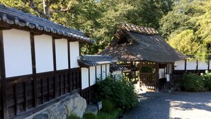 A traditional Japanese building with a thatched roof, surrounded by a gravel path and greenery. - Jonni’s Place (Otsu)