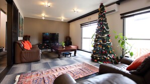 A living room with a large Christmas tree, leather sofas, a flat-screen TV, and a patterned rug. - Jonni’s Place (Otsu)
