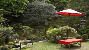 A traditional Japanese garden with a stone path, a wooden bench, and a red umbrella. - Jonni’s Place (Otsu)