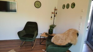 Een woonkamer met een groene fauteuil, een houten salontafel met een vaas, en een vloerlamp.