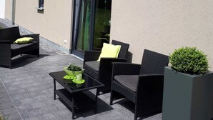 Un patio al aire libre con mobiliario de mimbre, una mesa de vidrio y plantas en macetas.