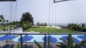 A pool area with blue umbrellas and lounge chairs, a grassy lawn, and a view of the ocean. - Trincomalee Beach Resort & spa (Trincomalee)