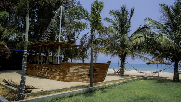 A beach scene with a wooden boat structure, palm trees, and a hammock. - Trincomalee Beach Resort & spa (Trincomalee)