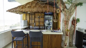 A bar area with a thatched roof, a refrigerator, shelves with glassware, and a large tree with hanging decorations. - Trincomalee Beach Resort & spa (Trincomalee)