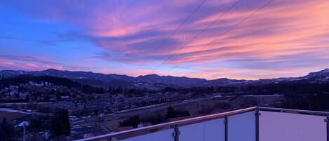 A balcony with a view of a town and mountains during sunset.