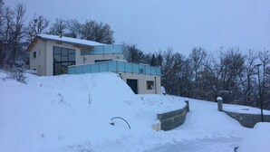 Moderni talo, jossa on kalteva katto ja suuret ikkunat, ja sen ympärillä on lunta.