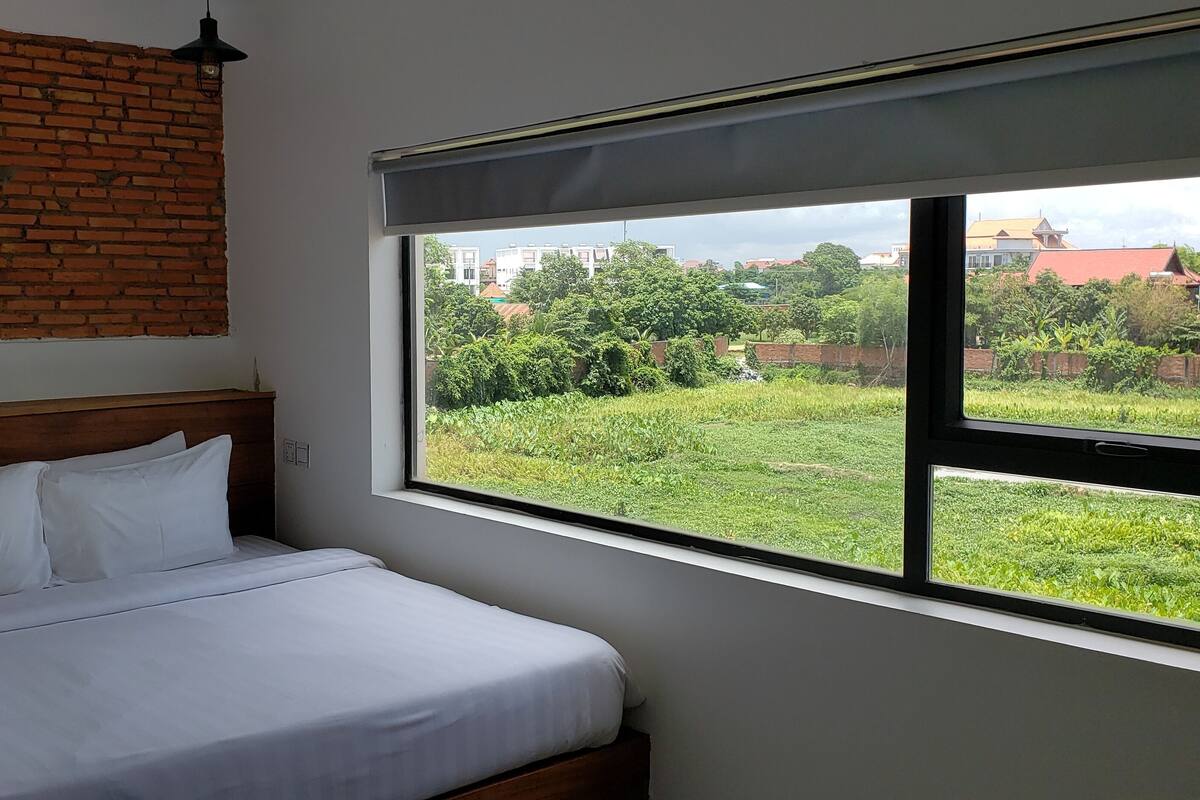 Un dormitorio con pared de ladrillo, un ventanal grande y una cama con ropa blanca.