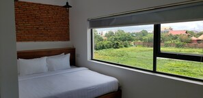 Une chambre avec un mur en briques, une grande fenêtre et un lit recouvert de linge de lit blanc.