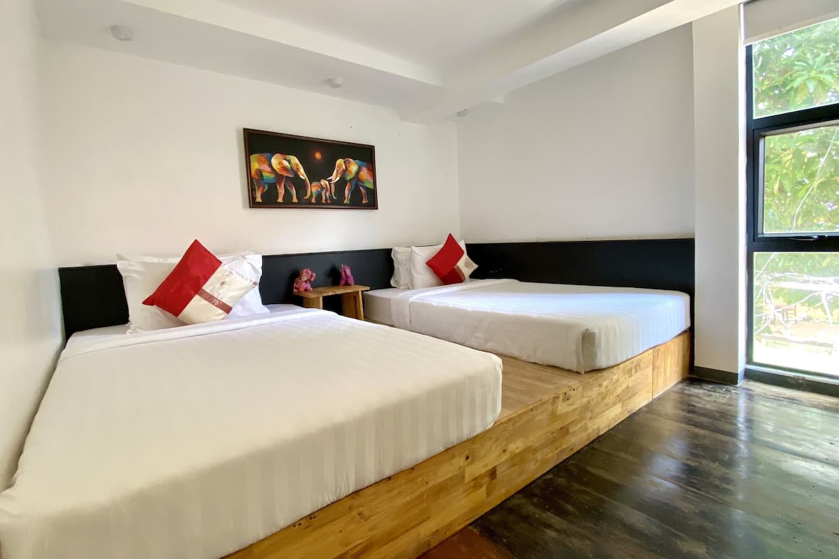 Habitación de hotel con dos camas, una plataforma de madera, un cuadro en la pared y un ventanal grande.