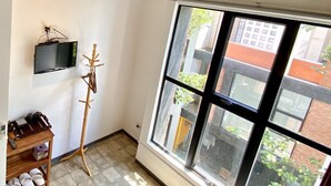 Une pièce dotée d’une grande fenêtre, de poutres apparentes en bois au plafond, d’un téléviseur et d’un meuble à chaussures.