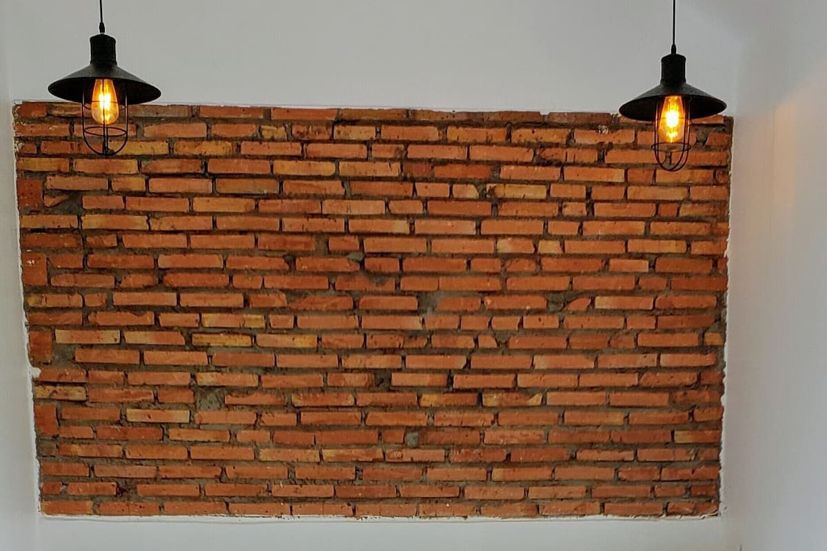 Una cama con cabecera de madera, ropa de cama blanca y una pared con diseño de ladrillo encima.