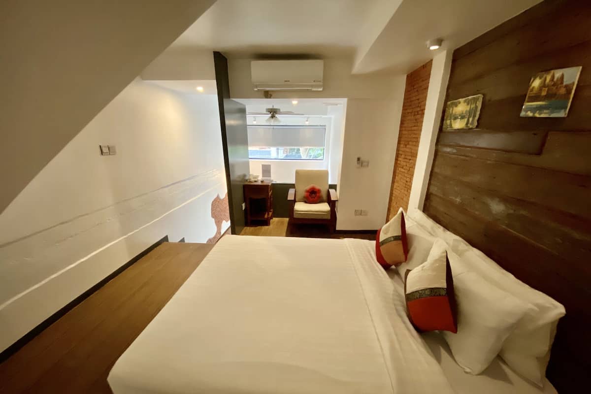 Habitación de hotel con una cama grande, una silla, una mesita y ventana con vistas.