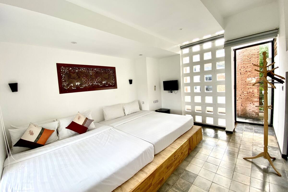 Un dormitorio moderno con una cama grande, una plataforma de madera, un televisor y un adorno en la pared.