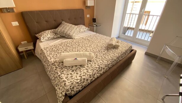 Een slaapkamer met een groot bed, een nachtkastje, een stoel en een raam met uitzicht.