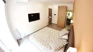 Een slaapkamer met een bed, een aan de muur bevestigde televisie, een kledingkast en een spiegel.