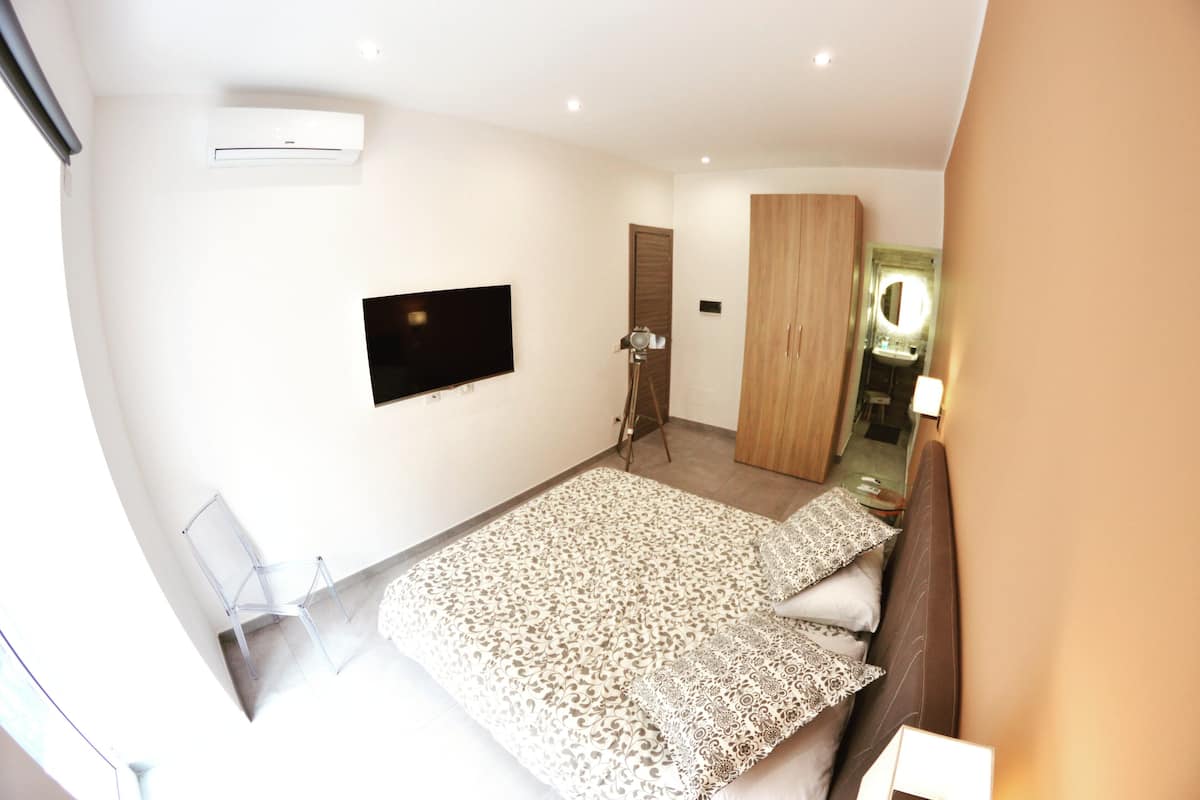 Une chambre à coucher comprenant un lit, un téléviseur fixé au mur, une armoire et un miroir.