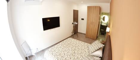 A bedroom with a bed, a TV mounted on the wall, a wardrobe, and a mirror.