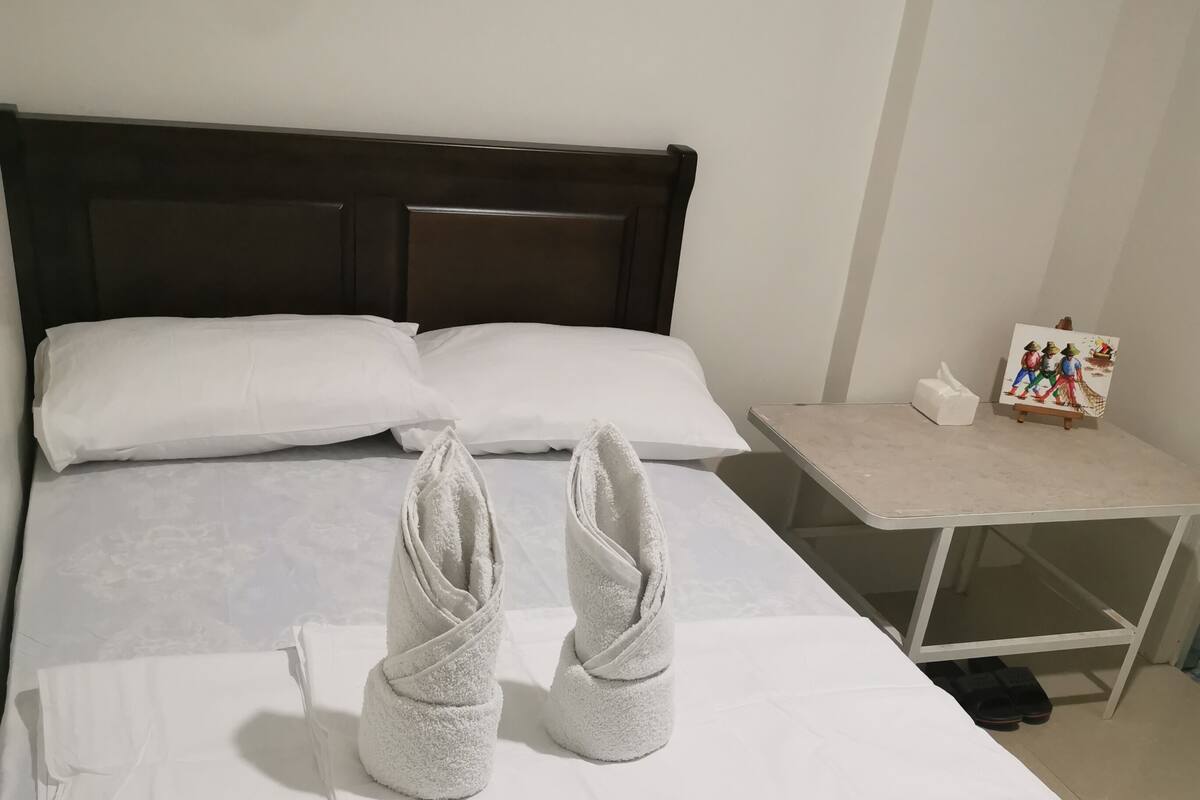 En snyggt bäddad säng med vita lakan och två handdukar prydligt vikta ovanpå.