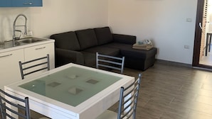 A modern living space with a dining table, chairs, a sofa, and a kitchen area with cabinets and a sink. - Modern apartment in the historic center of Orosei 70 M² - French Alps  (OROSEI)