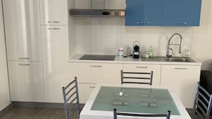 A modern kitchen with white and blue cabinets, a stainless steel range hood, a built-in sink, and a glass-top dining table with four chairs. - Modern apartment in the historic center of Orosei 70 M² - French Alps  (OROSEI)