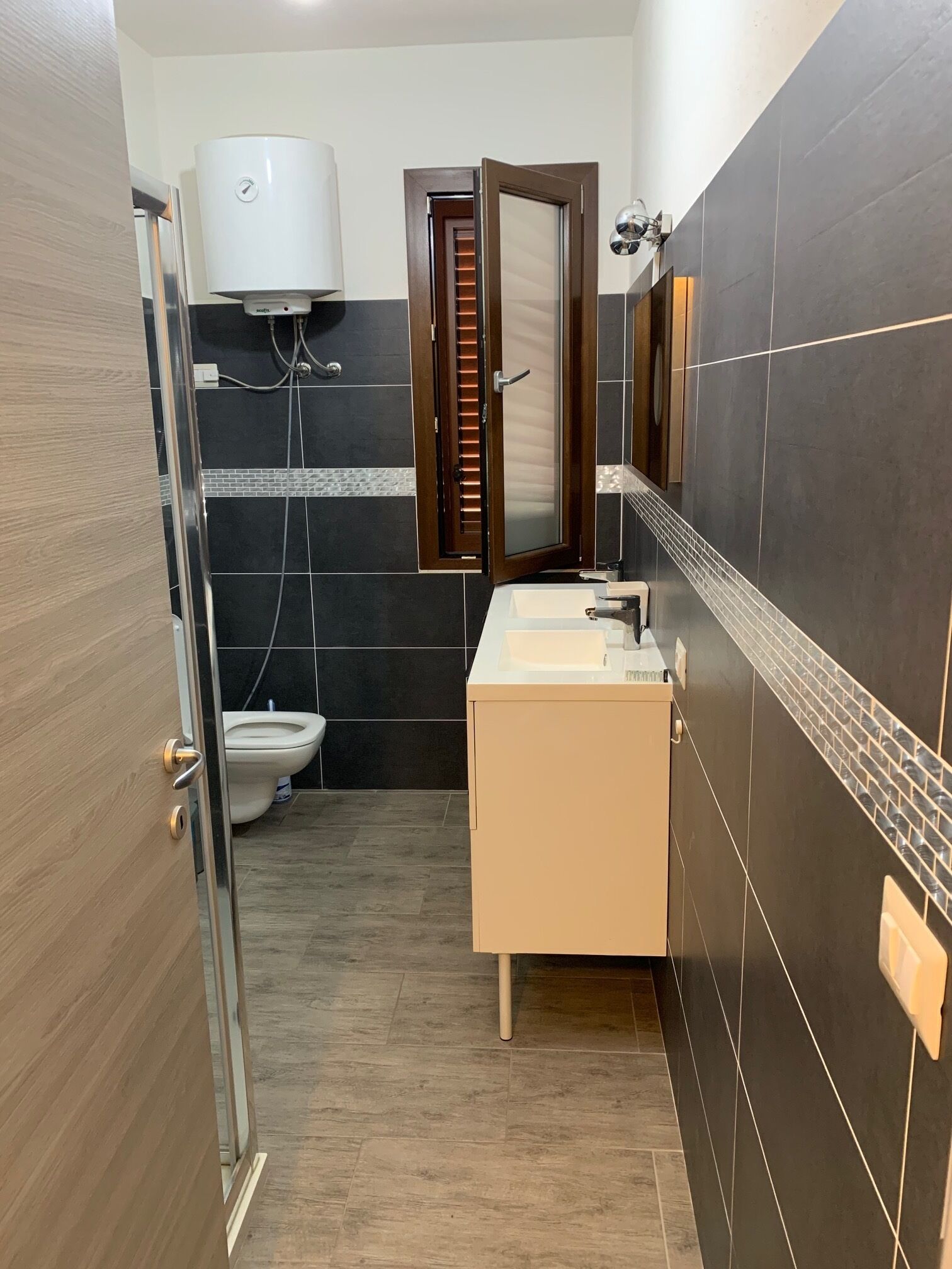 Et badeværelse med toilet, håndvask, spejl og bruseområde.